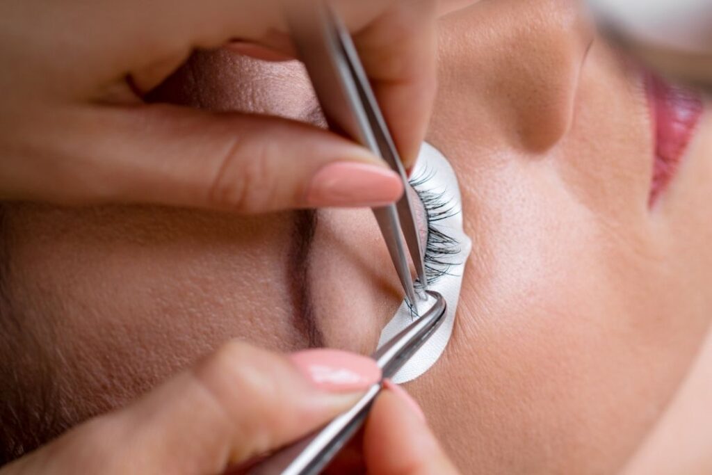 Kosmetikerin öffnet Wimpern mit einer Pinzette, um während einer Wimpernverlängerung weitere Wimpern anzubringen.