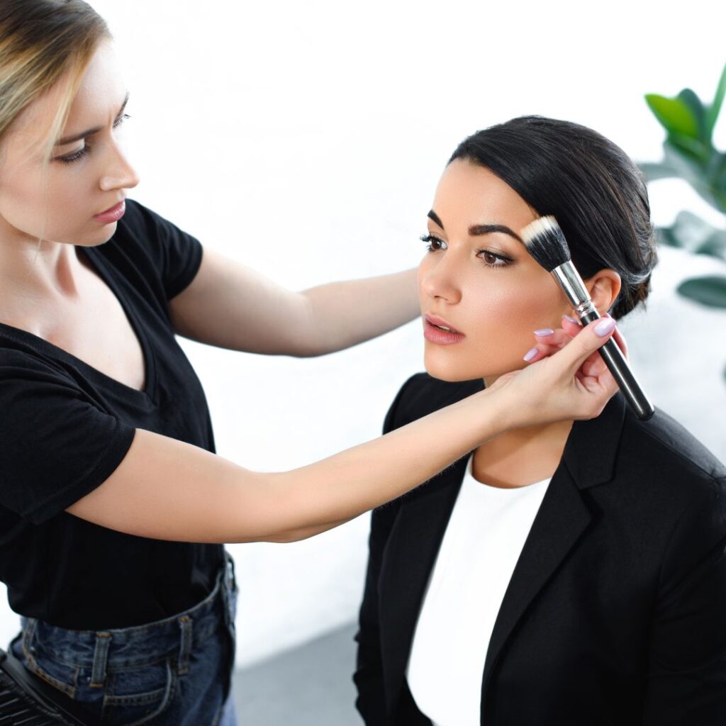 Lehrling setzt einen Pinsel am Gesicht des Modells an, während er in einer Make-up-Schulung übt.