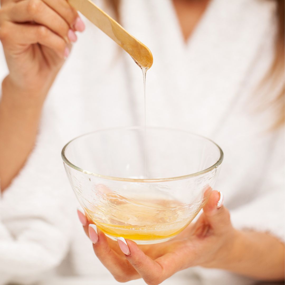 Schüssel mit Sugaring-Paste, die mit einem Holzstäbchen in die Höhe gezogen wird.